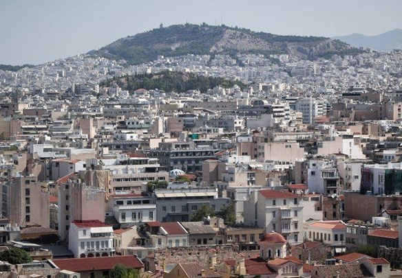Πανοραμική άποψη της πόλης της Αθήνας με πυκνή δόμηση και στο βάθος λόφος με πράσινο.